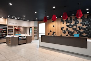 Un espace d’accueil d’hôtel au design moderne, comprenant un comptoir d’accueil, un minibar et un présentoir des équipements et services proposés.
