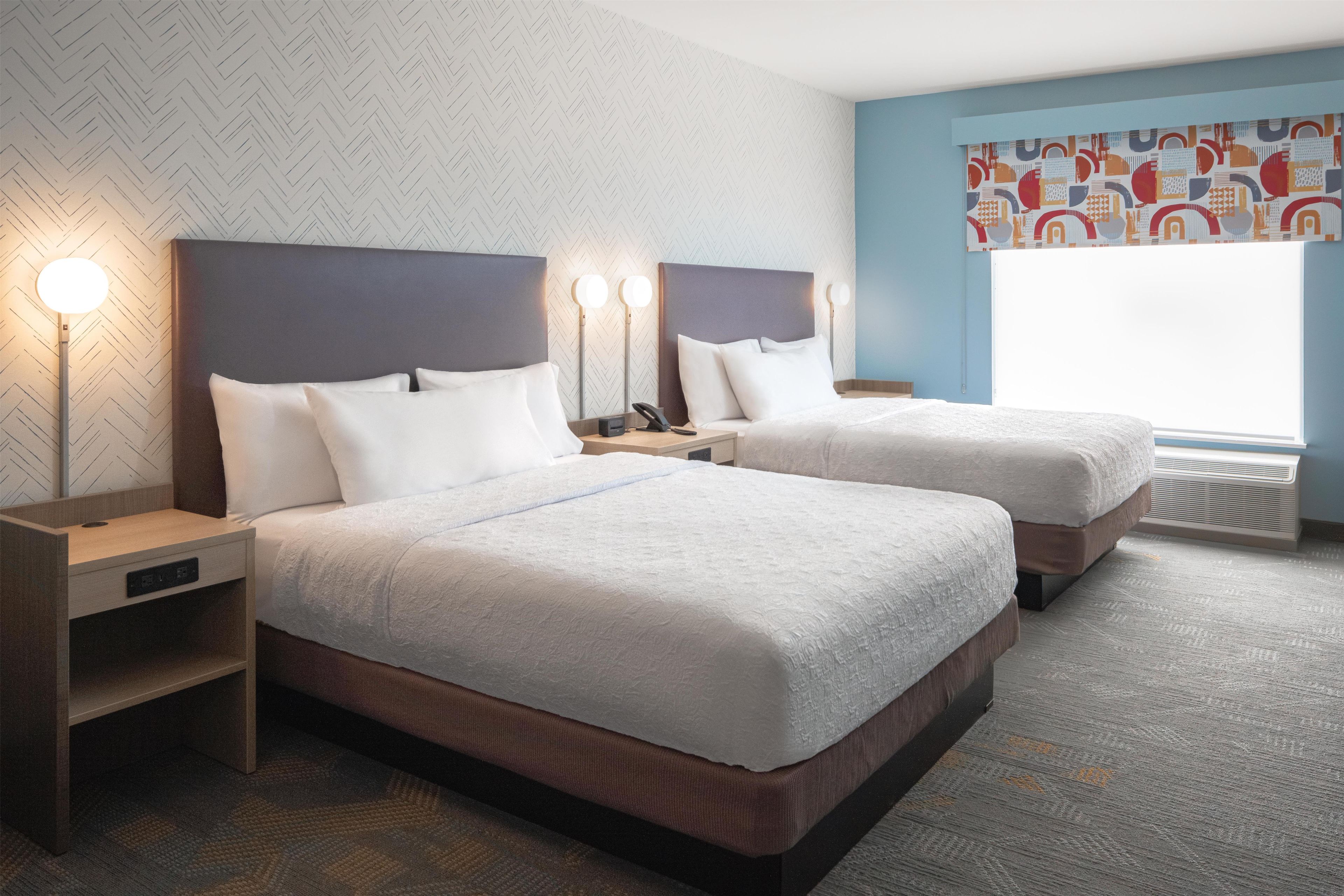 Een hotelkamer met twee bedden, een nachtkastje, een lamp en een raam met uitzicht.