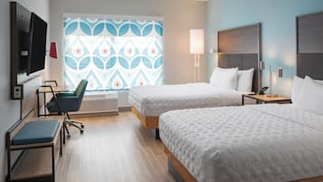 A hotel room with two beds, a desk, a chair, a TV, and a patterned window.