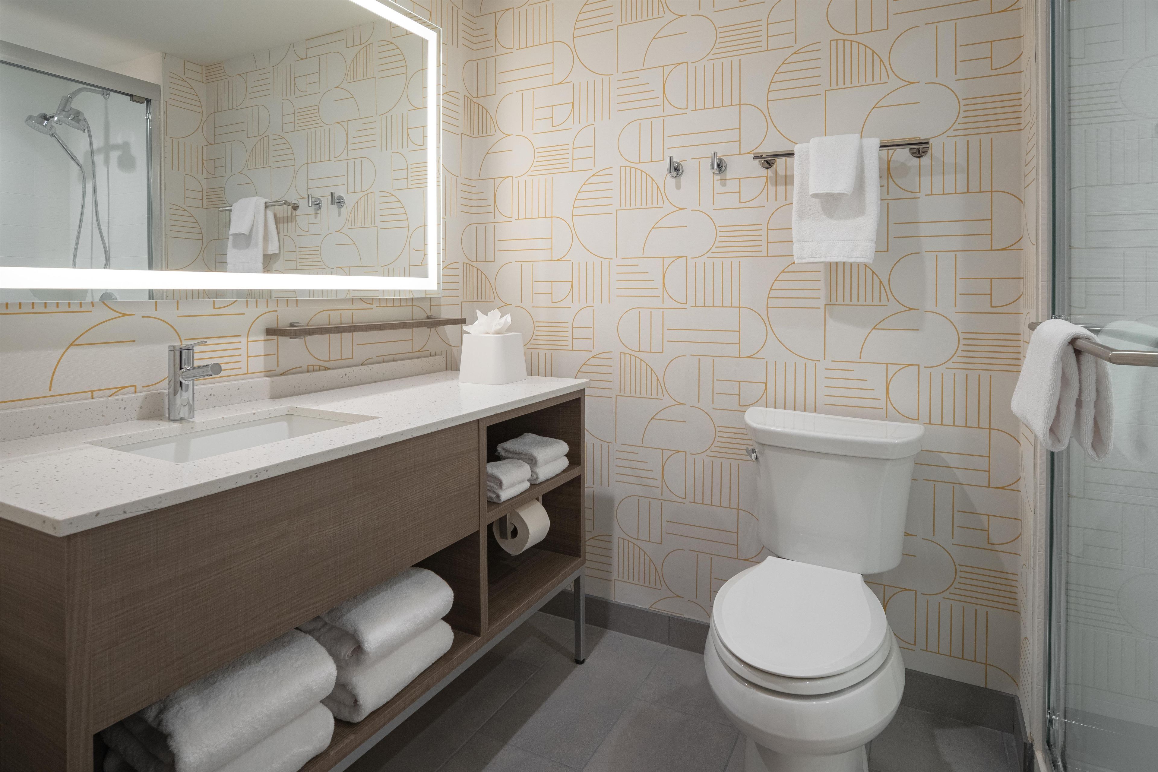 A modern bathroom with a large mirror, a sink, a toilet, and a shower.
