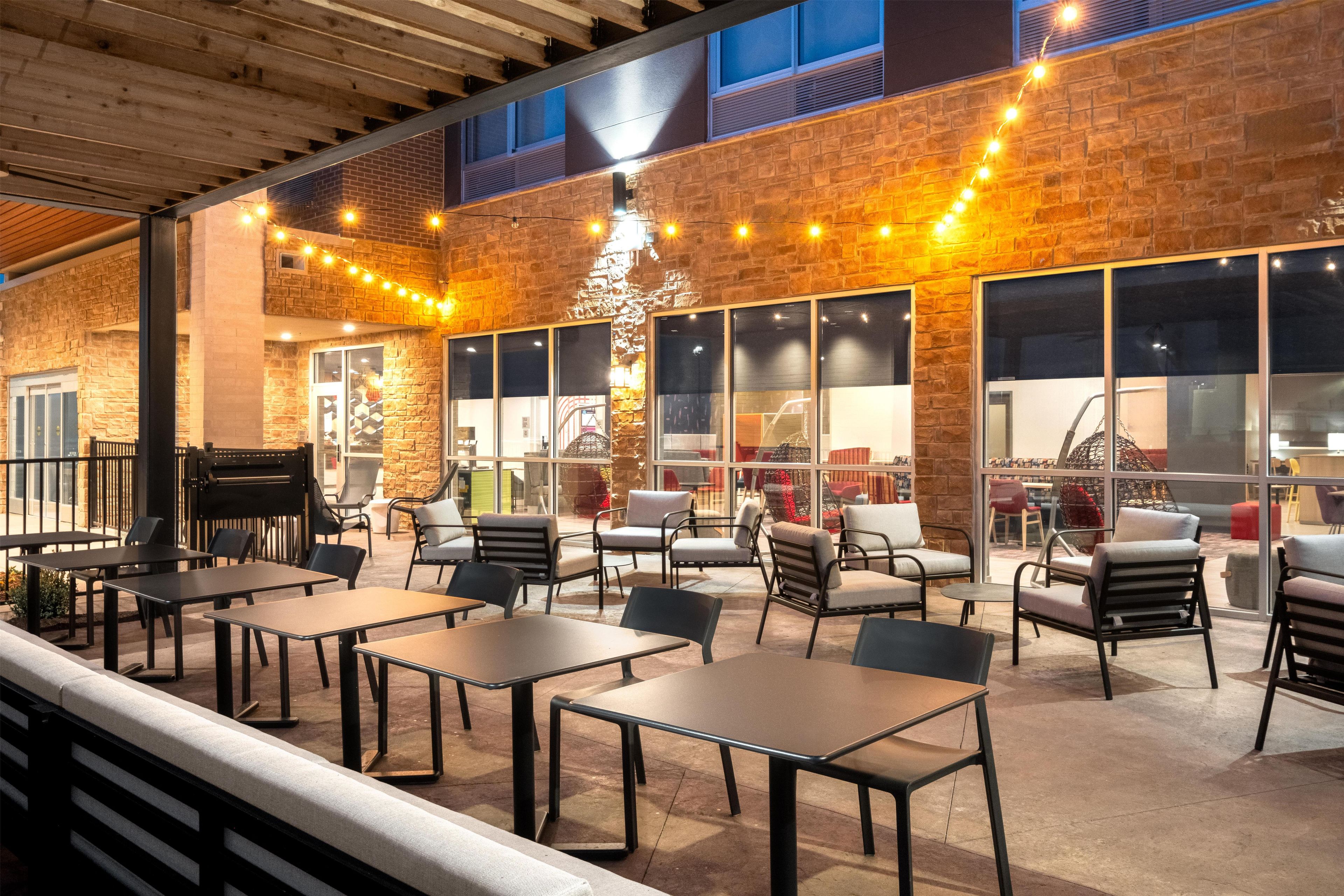 An outdoor seating area with tables and chairs, a piano, and string lights.