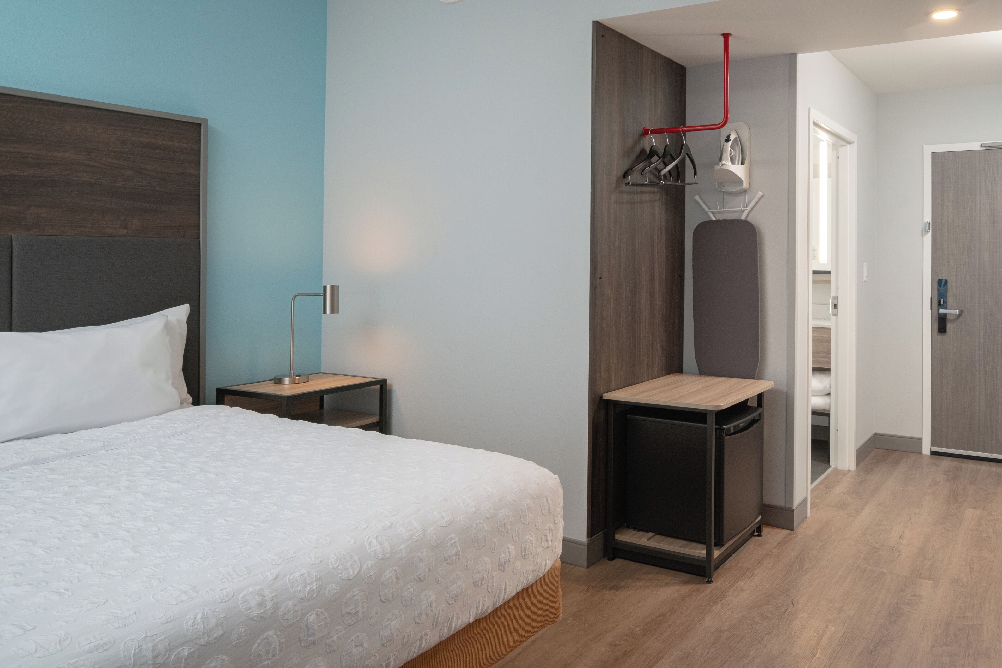 A modern bedroom with a large bed, a bedside table, a small desk, and a wardrobe.