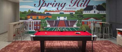 A pool table in a room with a mural of Spring Hill, Tennessee, and a bar area.