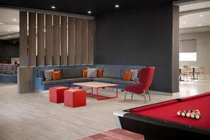 Un espace de détente moderne comprenant une table de billard, un canapé d’angle et un fauteuil rouge.