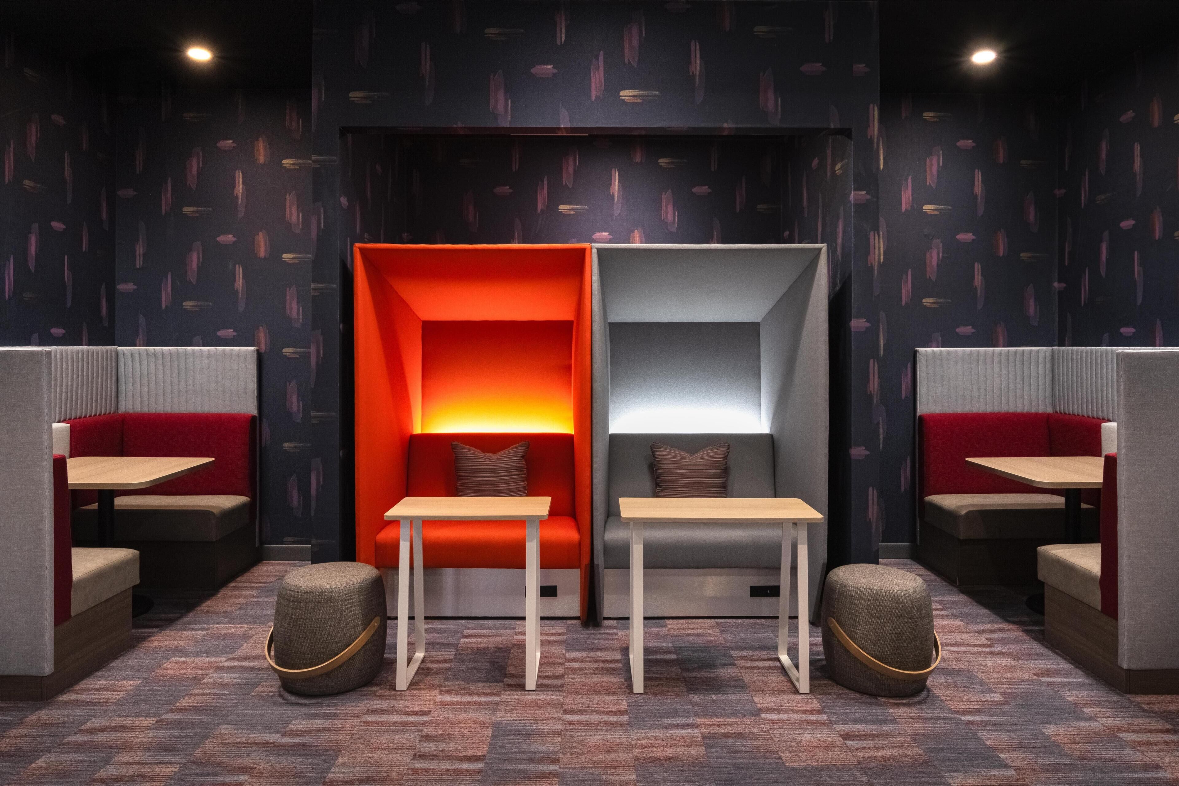 A modern lounge area with seating and tables, patterned wallpaper, and a dark ceiling.