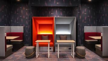 A modern lounge area with seating and tables, patterned wallpaper, and a dark ceiling.