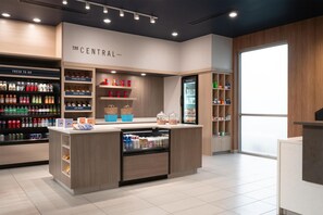 A modern retail space with a central counter, refrigerated display, and shelves stocked with beverages and snacks. - Tru By Hilton Spring Hill (Spring Hill)