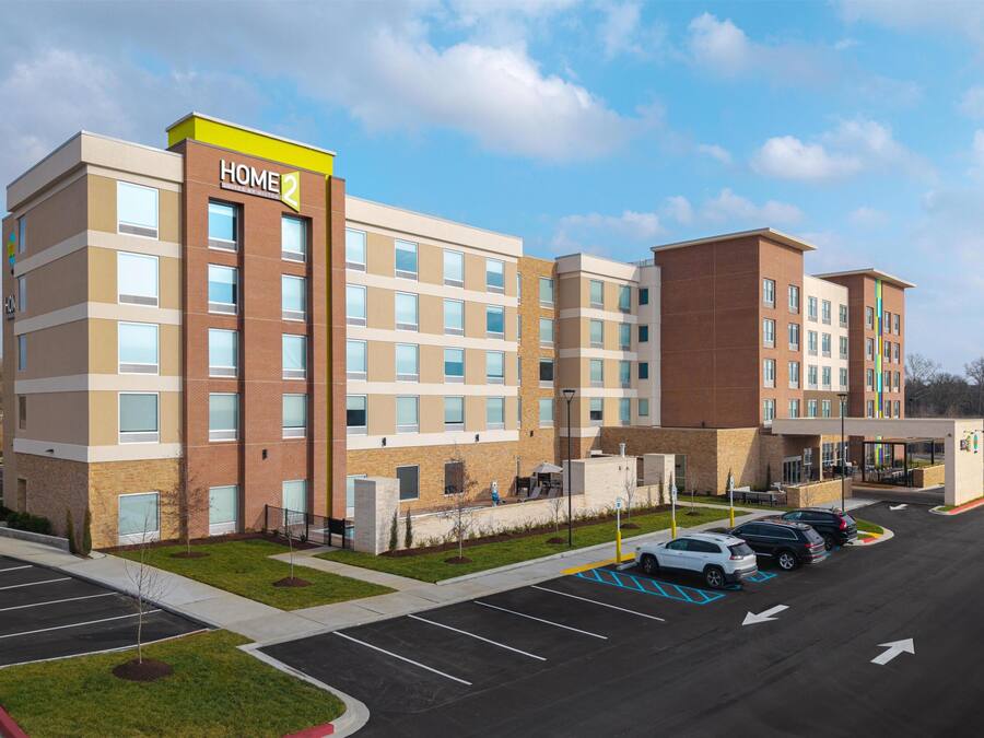 Un hotel de varios pisos con un letrero 'HOME2', estacionamiento y cielo despejado.