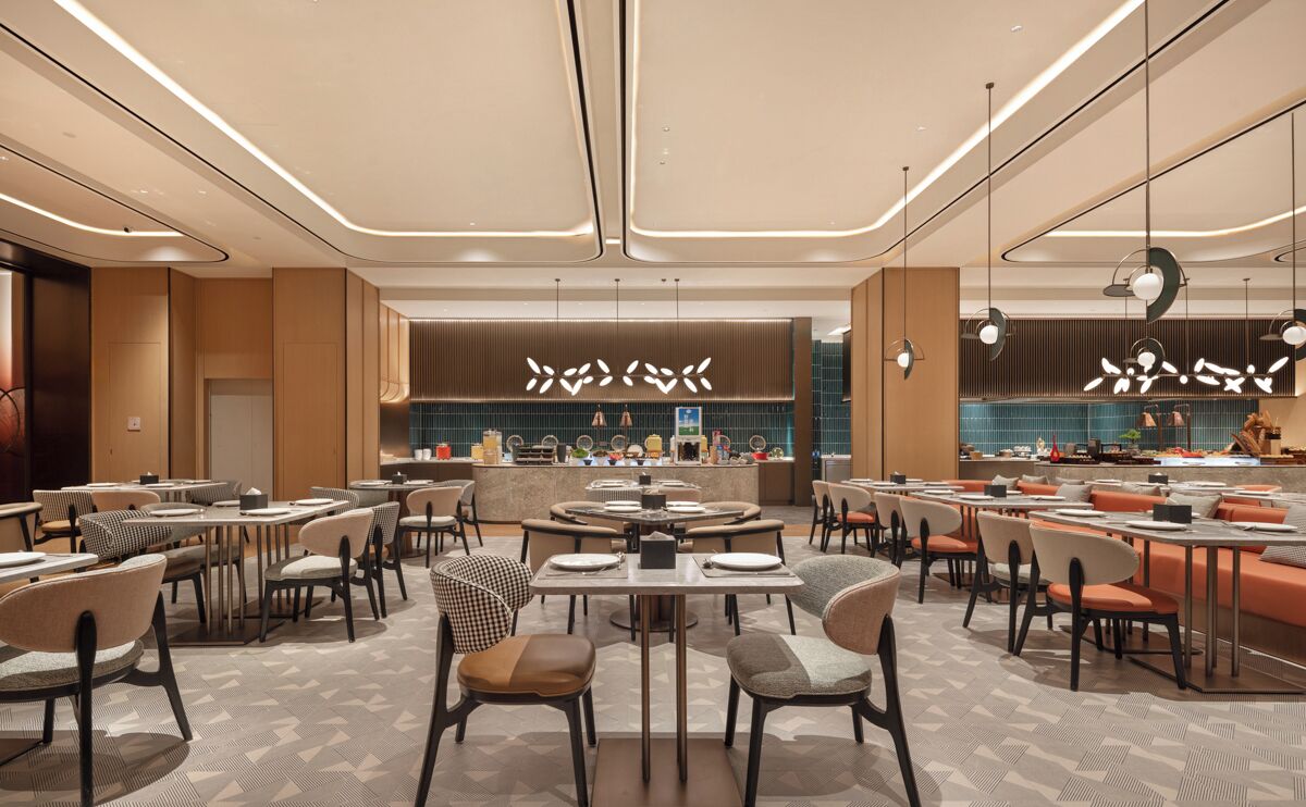 A modern hotel lobby with multiple dining areas, a central bar, and a reception desk.