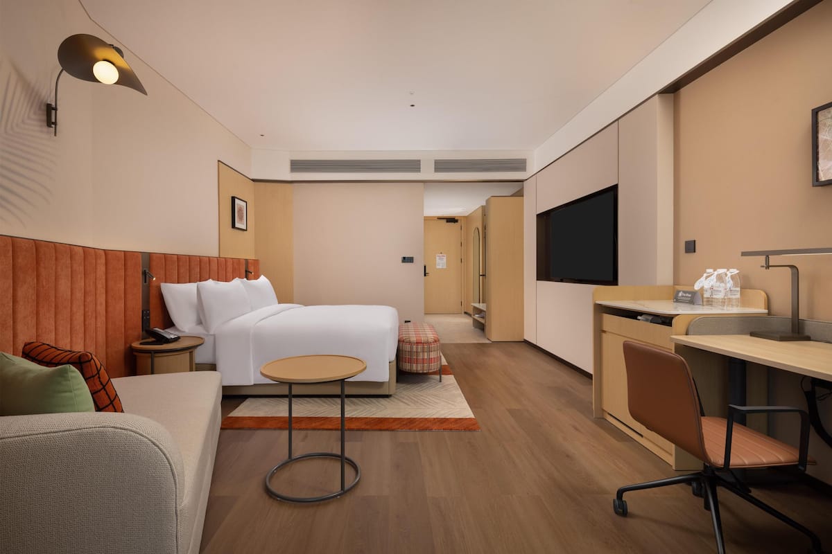 Una habitación de hotel moderna con una cama, un escritorio, una silla, una mesita y un televisor.
