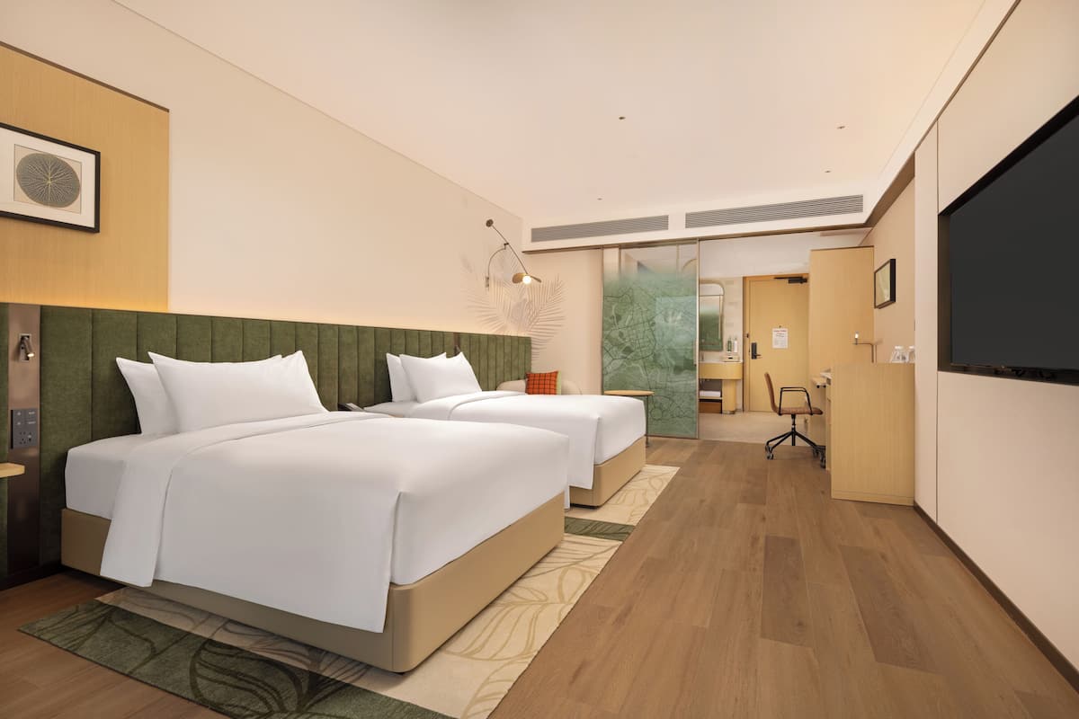 Habitación de hotel con dos camas, un escritorio, una silla y un televisor.