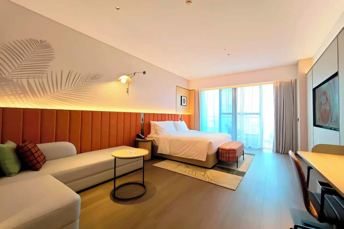 Una habitación de hotel moderna con cama, sofá, mesa redonda y un ventanal con cortinas.