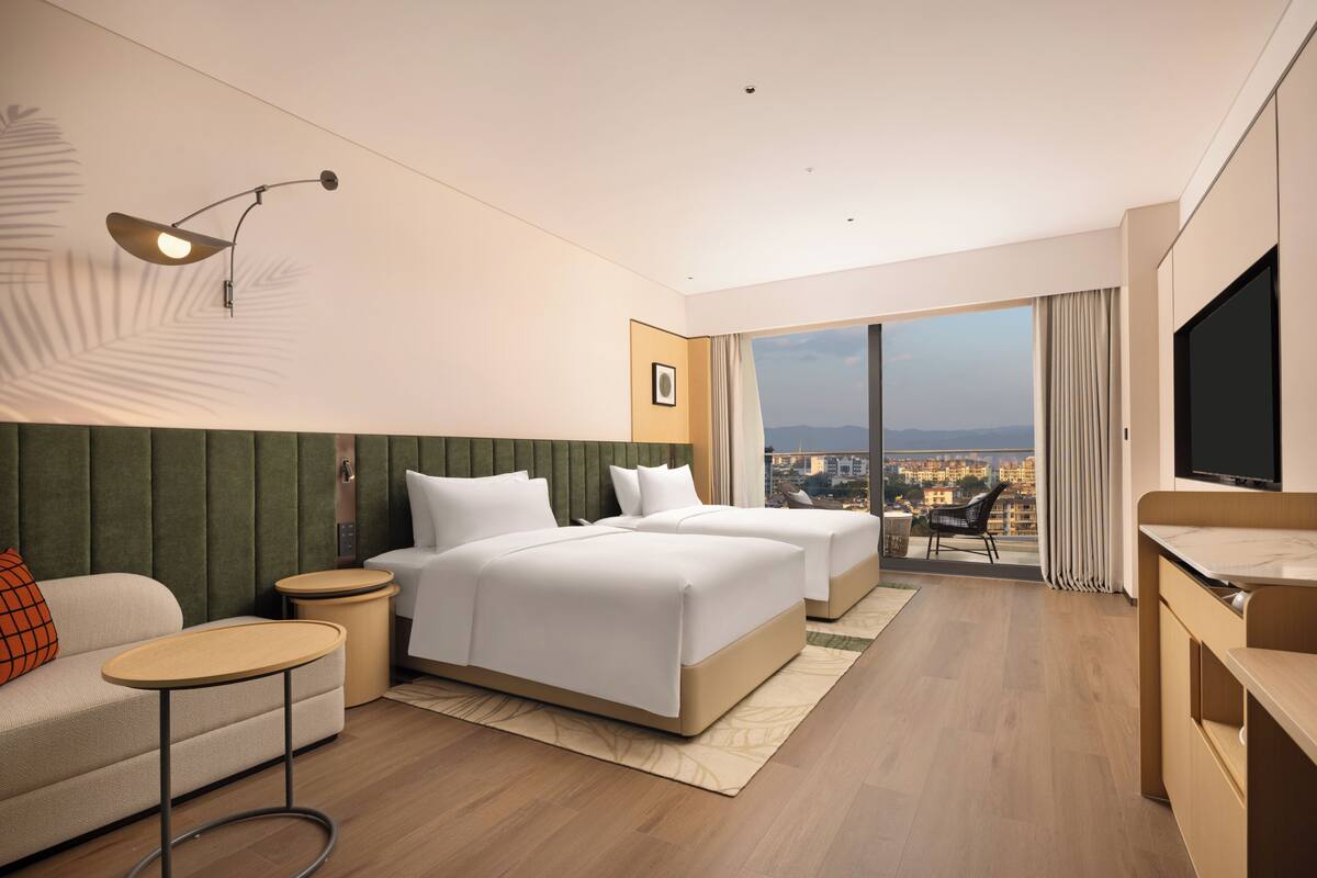 Una habitación de hotel moderna con dos camas, un sofá, un televisor y un balcón con vistas a la ciudad.