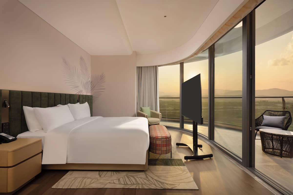 Una habitación de hotel moderna con una cama grande, un televisor de pantalla plana, una zona de estar con vistas a las montañas y un balcón con una silla.