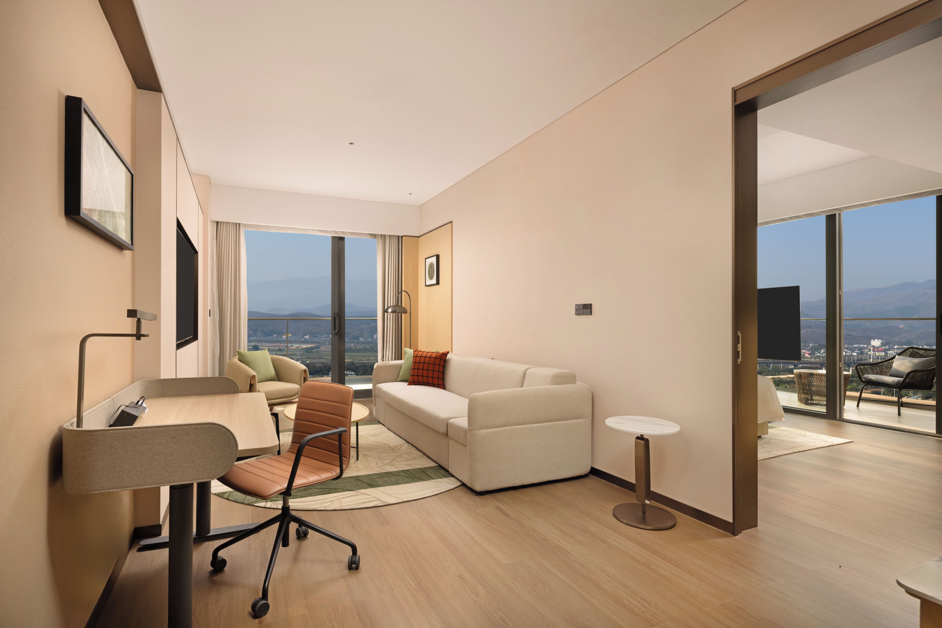 Una habitación de hotel moderna con un ventanal grande, un sofá, un escritorio y una silla.