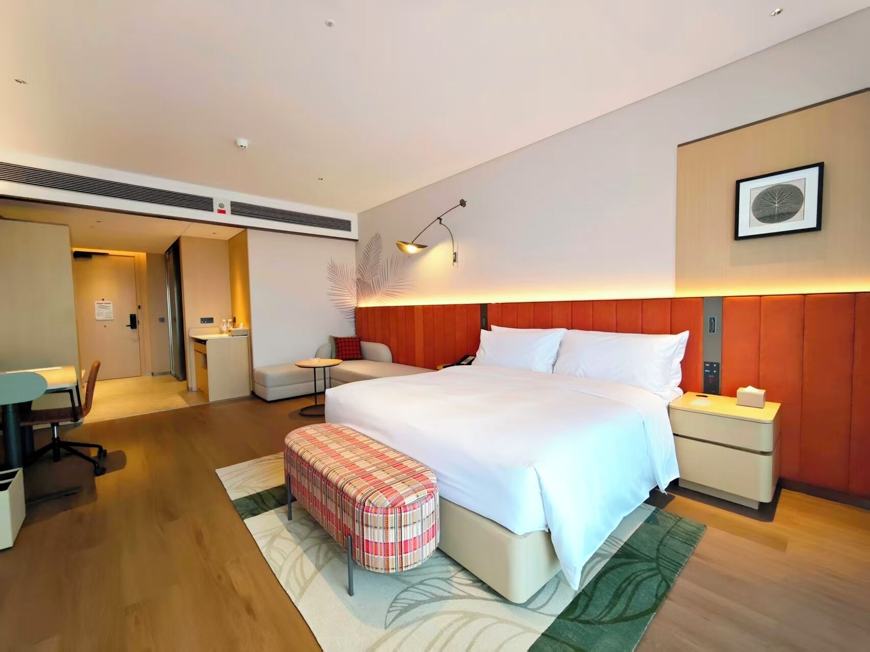 A modern hotel room with a large bed, bedside tables, a desk, and a bench.