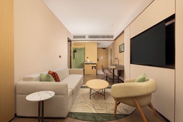 A hotel room with a sofa, a small round table, a chair, a TV, and a desk with a chair. - Hilton Garden Inn Xishuangbanna Railway Station (Xishuangbanna Dai)