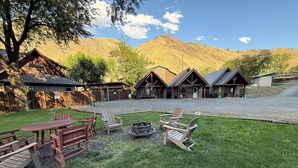A rustic lodge with wooden cabins, a grassy yard, and a mountain backdrop.