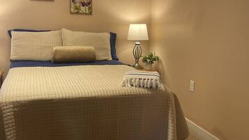 A bedroom with a bed, pillows, a bedside lamp, a small plant, and two floral wall art pieces.