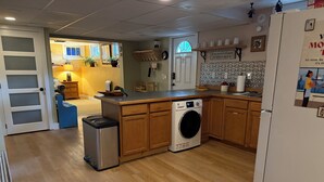 A compact kitchen with a washing machine, wooden cabinets, and a small refrigerator. - Steps from University –  3BR, Sleeps 6, FirePit Backyard Concerts & GameDay (Missoula)