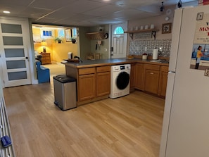 A compact kitchen with a washing machine, wooden cabinets, and a small refrigerator. - Steps from University –  3BR, Sleeps 6, FirePit Backyard Concerts & GameDay (Missoula)