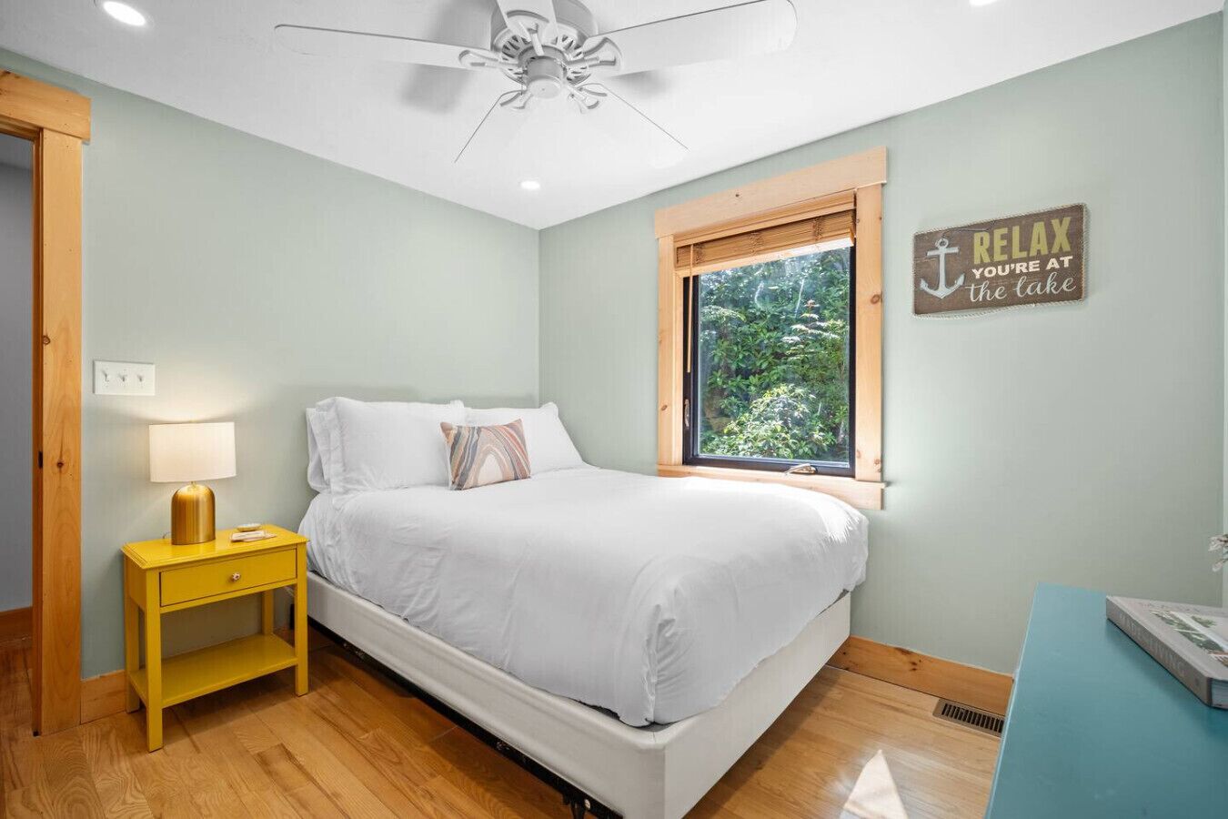 Una camera da letto con un letto, un comodino, una finestra che si affaccia sul verde e una ventola a soffitto.