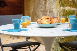 Une table ronde avec un panier de croissants, des verres de jus d’orange, des serviettes bleues et des tasses bleues assorties.