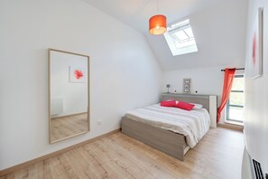 Une chambre à coucher avec un lit, un grand miroir, une lucarne et une fenêtre avec des rideaux.