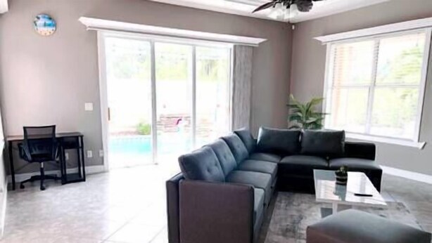Ein geräumiges Wohnzimmer mit einem Ecksofa, einem Couchtisch und einem kleinen Tisch mit einem Sessel. Eine Glastür führt zu einer Terrasse.
