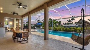 Amplo espaço interno com piscina, ventiladores de teto e área de refeições com cadeiras e mesa.