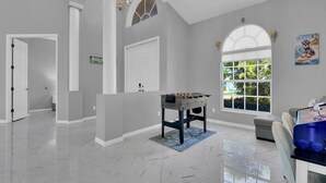Um quarto amplo com mesa de pebolim, uma janela grande com vista para o verde e um candelabro.