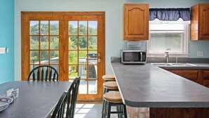 Cocina con una isla grande, armarios de madera, un microondas y una ventana con vistas a zonas verdes.