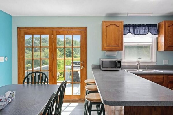 A kitchen with a large island, wooden cabinets, a microwave, and a window with a view of greenery.