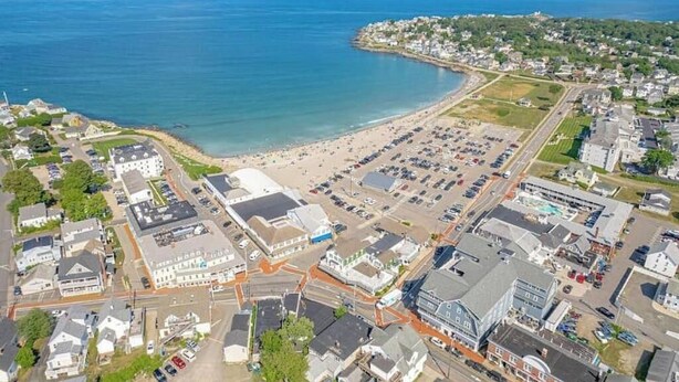 Vista aérea de un pueblo costero con playa, estacionamientos y edificios residenciales.