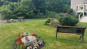 Un área verde bien cuidada con un elemento decorativo de piedra, un banco y una casa al fondo.
