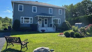 Una casa de dos pisos con un porche delantero, una banca y un césped bien cuidado.