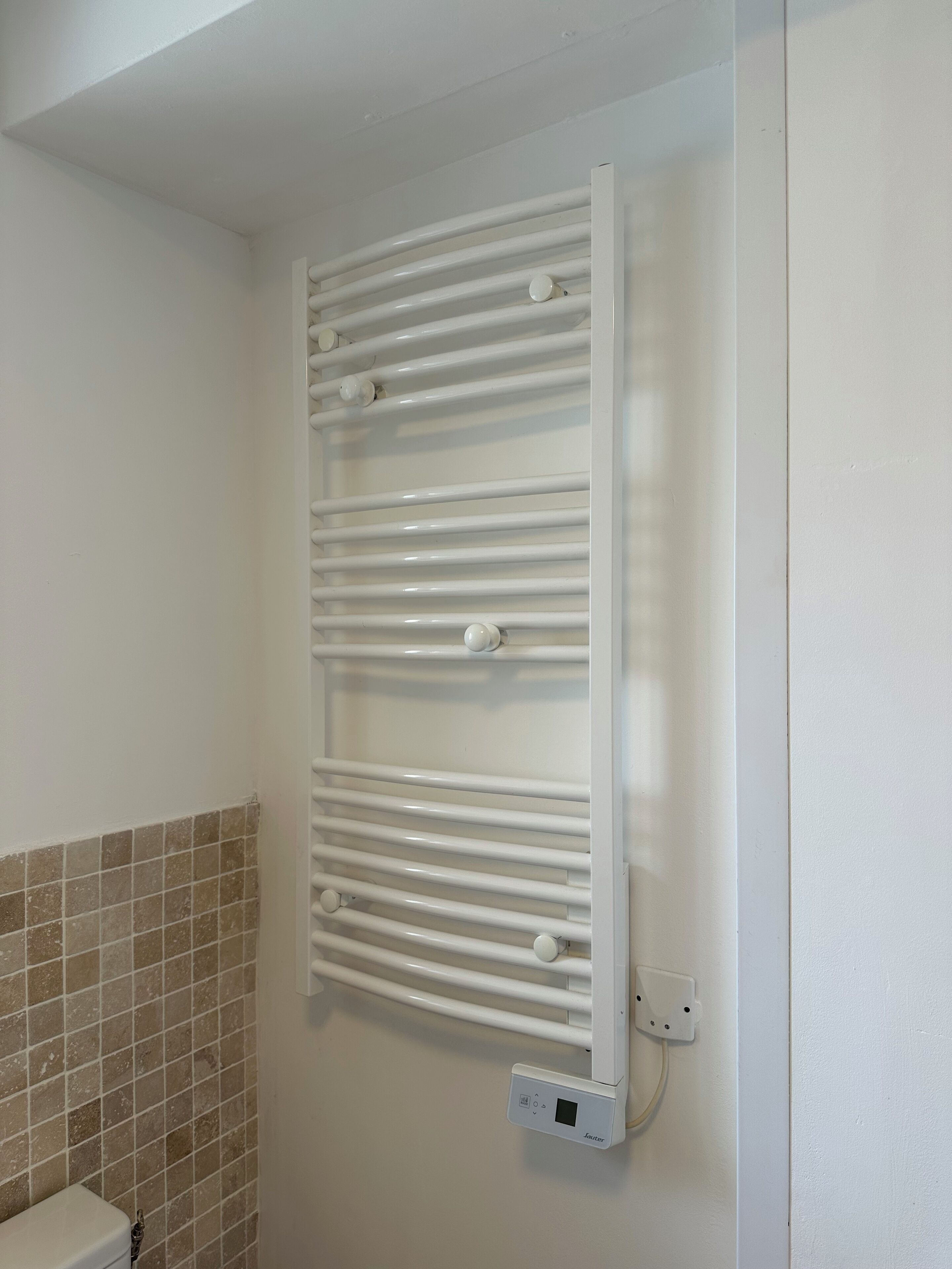 Une salle de bain avec un radiateur blanc, un mur carrelé et des toilettes blanches.