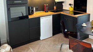 Una cocina moderna con armarios negros, encimera de madera, lavavajillas integrado y una mesa de comedor redonda con una silla.