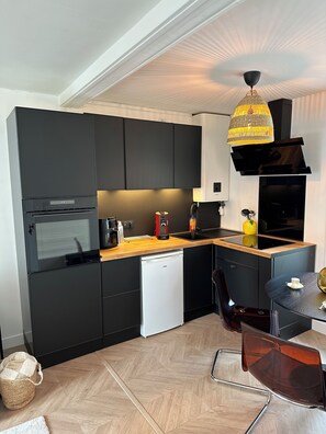 A modern kitchen with black cabinets, a wooden countertop, a built-in dishwasher, and a round dining table with a chair. - Gardiner - 200m to market square, 500m to beach (Dinard)