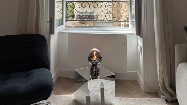 Una habitación con un ventanal grande, una silla negra, una mesita con un objeto decorativo y un sofá blanco.