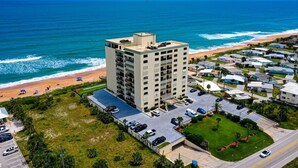 Een hoog hotel met meerdere verdiepingen, een parkeerplaats en uitzicht op het strand.