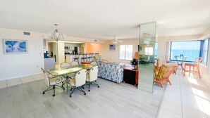 Een ruime woonkamer met een eettafel, stoelen, een bank en een grote spiegel die de kamer weerspiegelt.