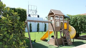 A wooden play structure with a slide and climbing area, surrounded by greenery and a white wall. - Excellent place to rest!!! (Cuernavaca)