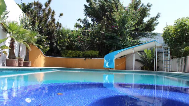 A swimming pool with a slide, surrounded by lush greenery and a white building. - Excellent place to rest!!! (Cuernavaca)