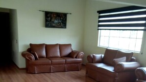 A spacious living room with a brown leather sectional sofa, a smaller armchair, and a large window with blinds. - Excellent place to rest!!! (Cuernavaca)