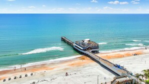 A pier extending into the ocean with a building on it, adjacent to a sandy beach.