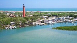 A coastal town with a prominent red lighthouse, marina with boats, and lush greenery.