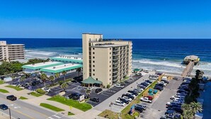 A hotel with a parking lot, a beach view, and a pool area.