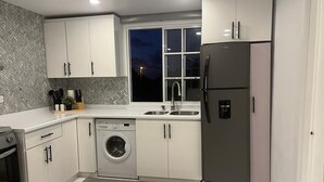 Eine moderne Küche mit weißen Schränken, einer integrierten Waschmaschine, einem Edelstahlkühlschrank und einem Fenster mit Blick ins Nachtlicht.