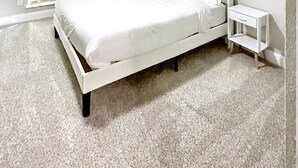 Une chambre à coucher comprenant un lit, une table de chevet, un ventilateur de plafond et une fenêtre avec des stores.